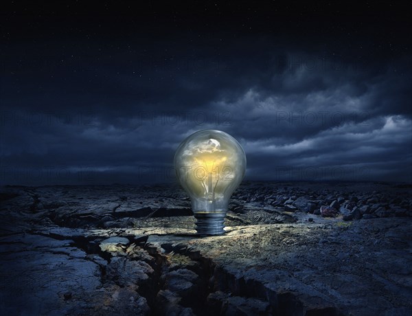 Illuminated light bulb in cracked earth