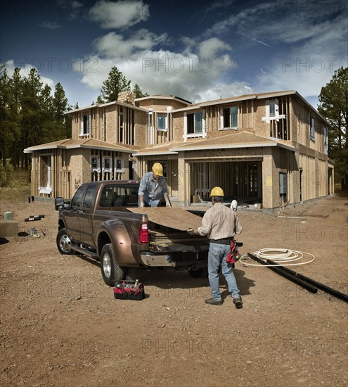 Construction workers carrying plywood on site