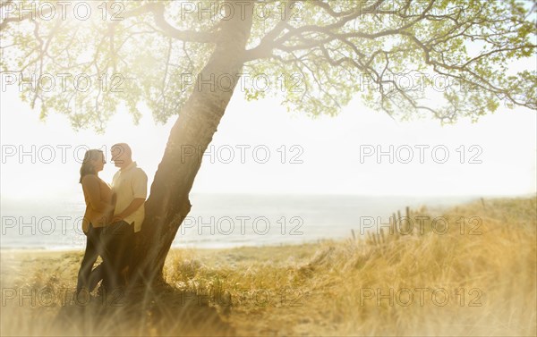 Caucasian couple hugging near tree in field