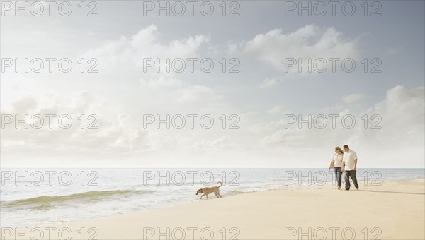 Caucasian couple walking dog on beach