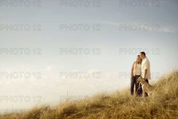 Caucasian couple walking dog on grassy dunes