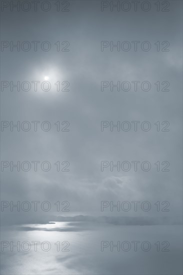 Sun shining in cloudy sky over ocean