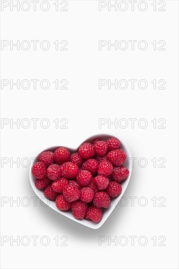 Raspberries in heart-shape bowl on white background