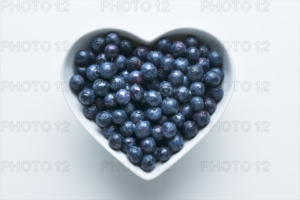 Blueberries in heart-shape bowl on white background