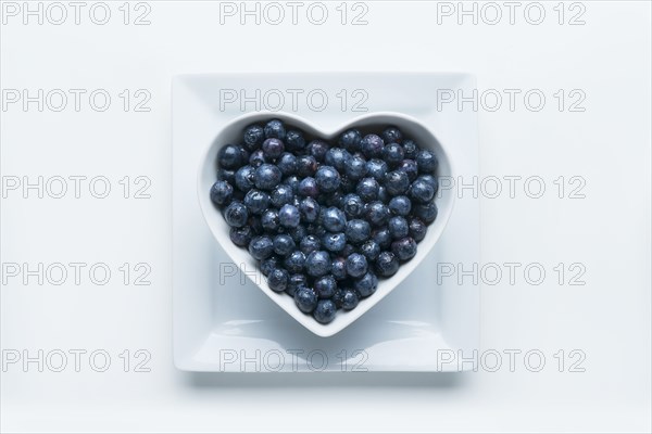 Blueberries in heart-shape bowl on white background