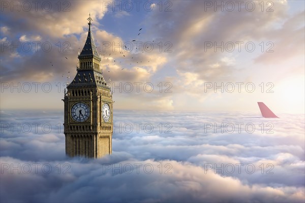 Birds flying around clock tower near airplane rudder above clouds