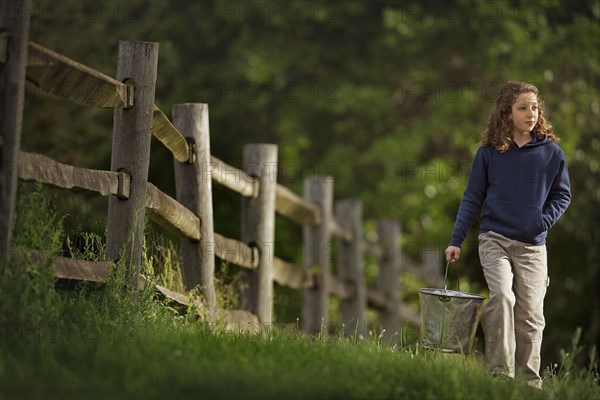 Caucasian girl carrying bucket near wooden fence