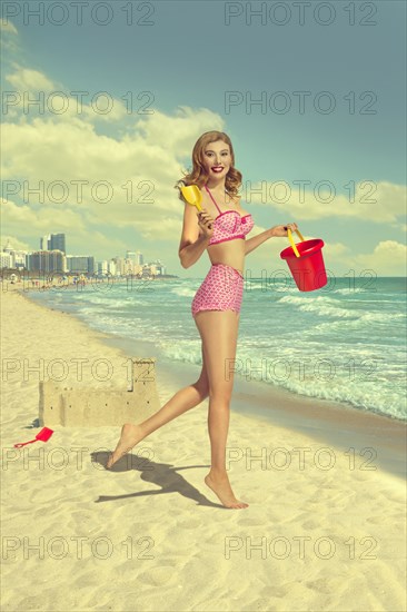 Caucasian woman running on beach carrying shovel and pail