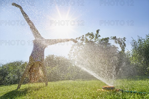 Caucasian girl performing cartwheel through backyard sprinkler