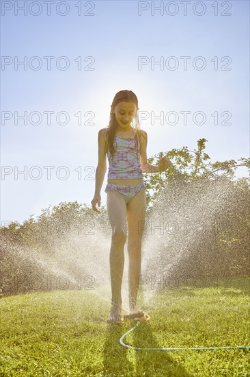 Caucasian girl standing over backyard sprinkler