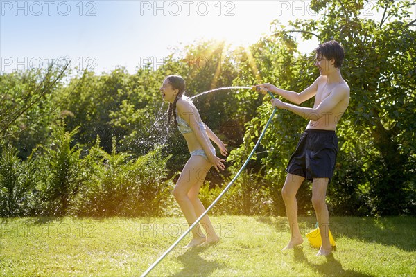 Caucasian boy spraying sister with hose in backyard