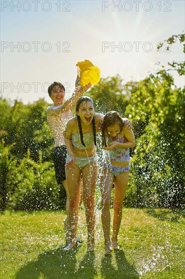 Caucasian boy dumping bucket of water on girls in backyard