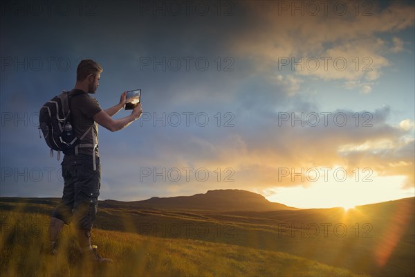 Caucasian hiker photographing sunset with digital tablet