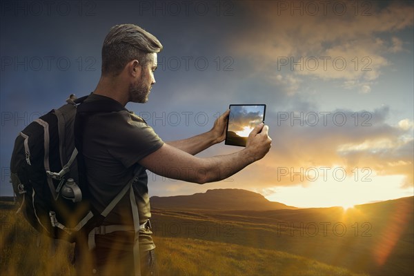 Caucasian hiker photographing sunset with digital tablet