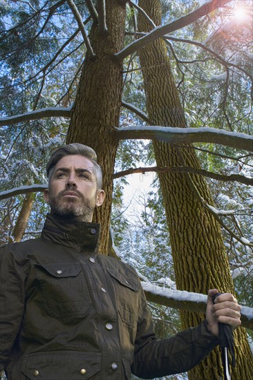 Caucasian hiker holding walking stick under snowy tree