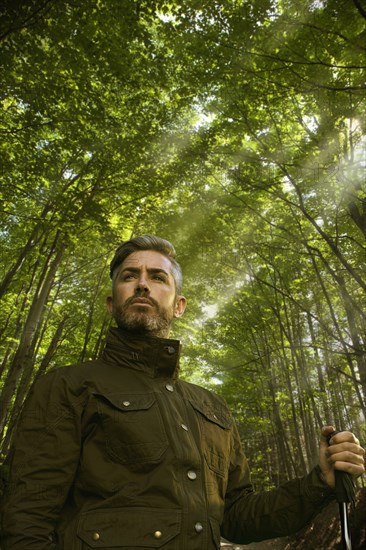 Caucasian hiker holding walking stick under sunny trees