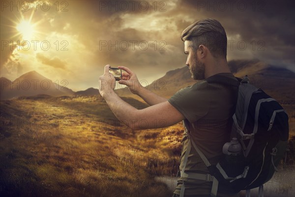 Caucasian hiker photographing mountain sunset with cell phone