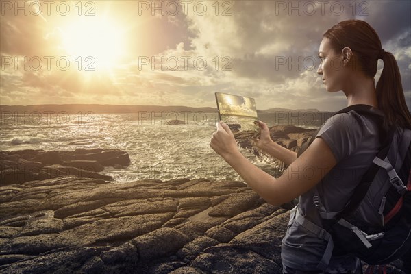 Caucasian woman photographing ocean sunset with digital tablet