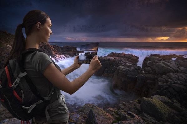 Caucasian woman photographing ocean sunset with digital tablet