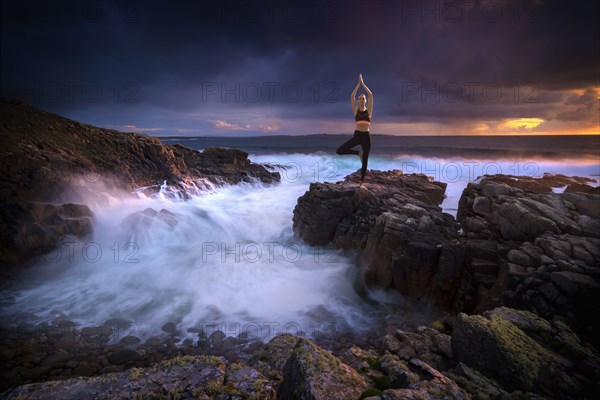 Distant Caucasian woman doing yoga on rocks near ocean