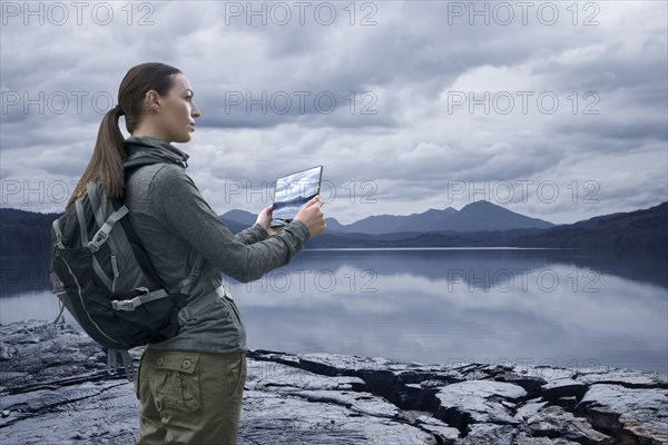 Caucasian woman photographing mountain lake with digital tablet
