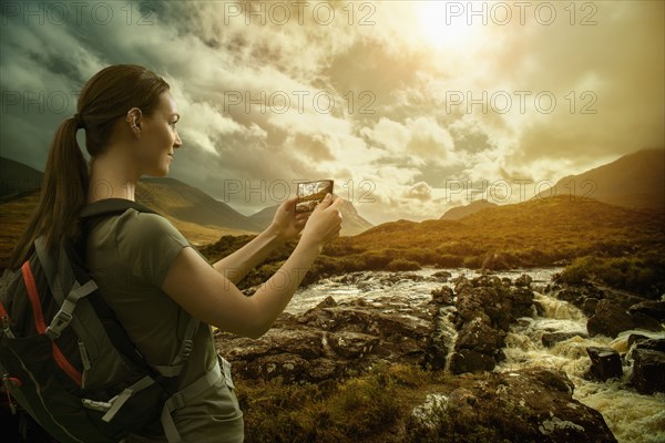 Caucasian woman photographing mountain river with cell phone