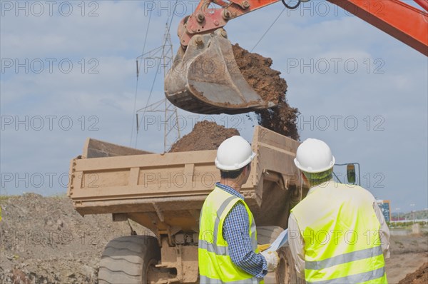 Hispanic construction workers watching dirt falling into dump truck