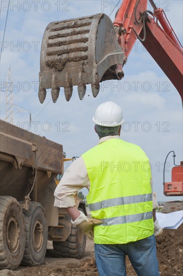 Hispanic construction worker watching backhoe