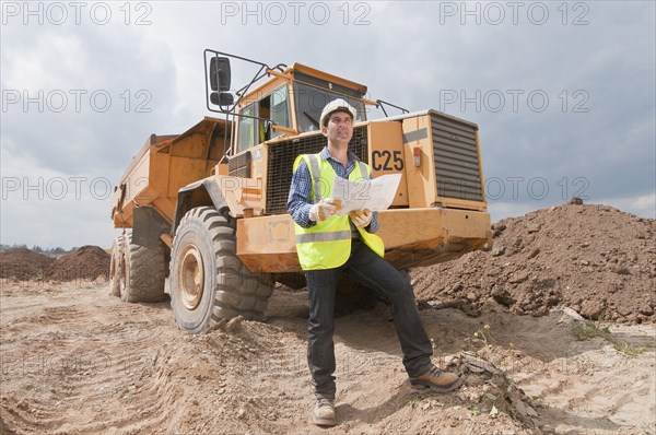 Hispanic construction worker with blueprints near dump truck