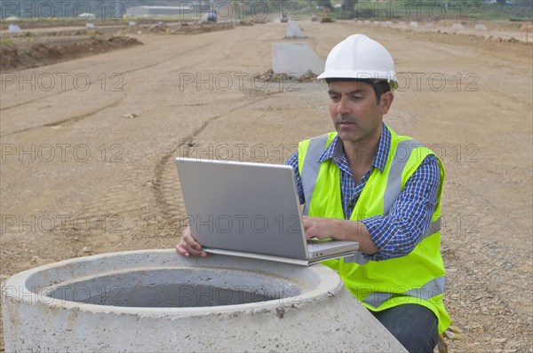 Hispanic construction worker using laptop in field