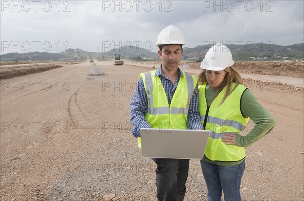 Hispanic construction workers using laptop in field