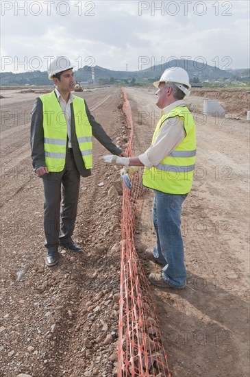 Hispanic businessman and construction worker standing in field