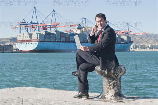 Hispanic businessman holding laptop with container ship in background