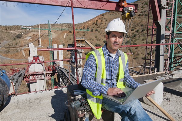 Hispanic construction worker using laptop at construction site