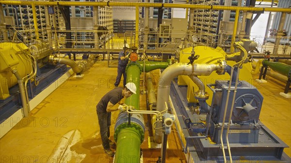 Hispanic workers examining pipes in factory