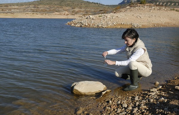 Female scientist taking water sample from lake side view