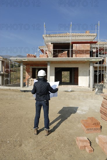 Female architect on construction site looking at plan rear view