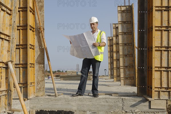 Male engineer wearing hard hat looking at plans on building site