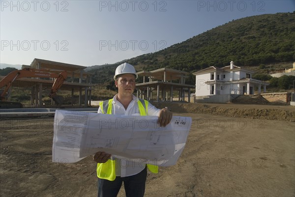 Male engineer wearing hard hat looking at plans on building site