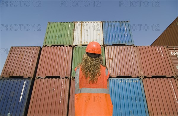 Woman wearing hard hat standing by containers in dock rear view