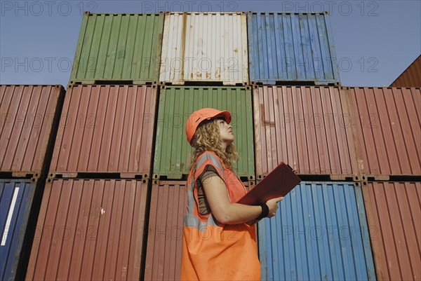Female worker with clipboard in cargo container terminal low angle