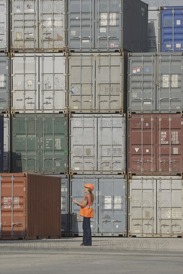 Female worker with clipboard in cargo container terminal low angle