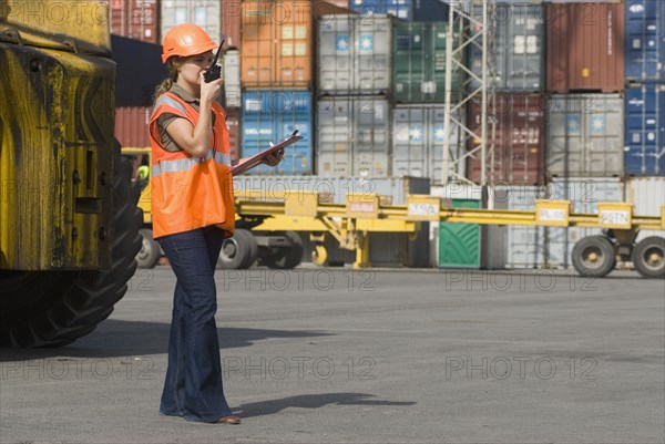 Woman wearing hard hat using walkie-talkie at container terminal