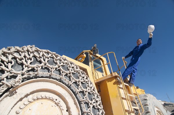 worker waving hard hat standing on mining machine