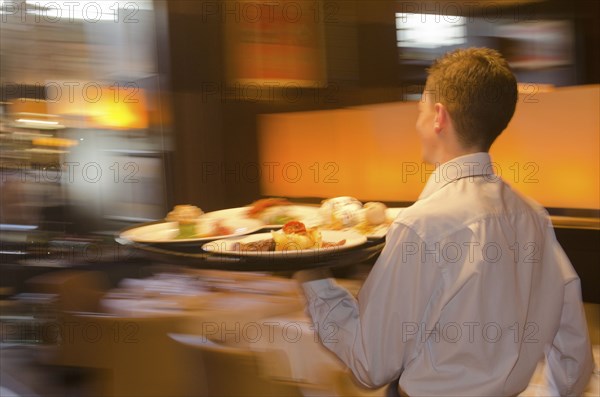 Waiter carrying tray with dishes through resturant