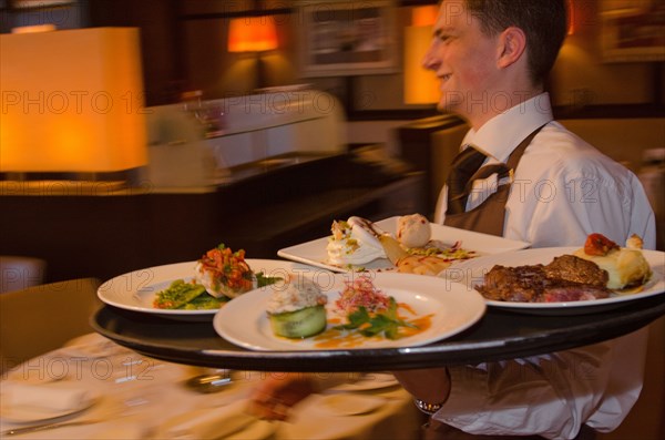 Waiter carrying tray with dishes through resturant