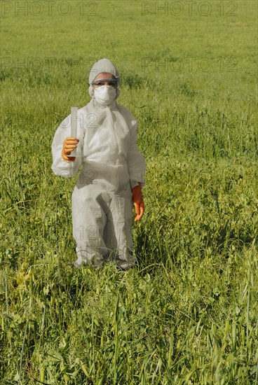 Woman in boiler suit standing in field holding test tube