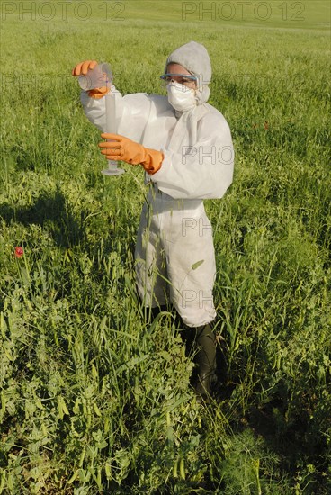 Woman in boiler suit standing in field pouring liquid into test tube