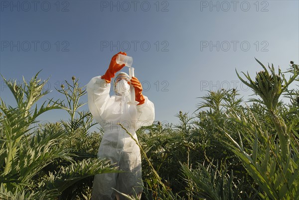 Woman in boiler suit standing in field pouring liquid into test tube