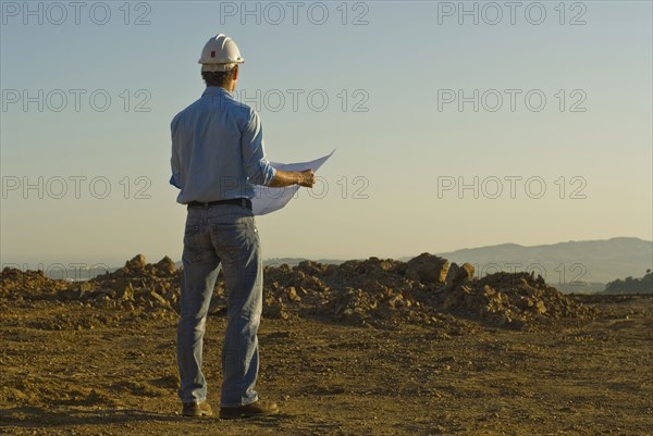 Young engineer with plan on construction site rear view